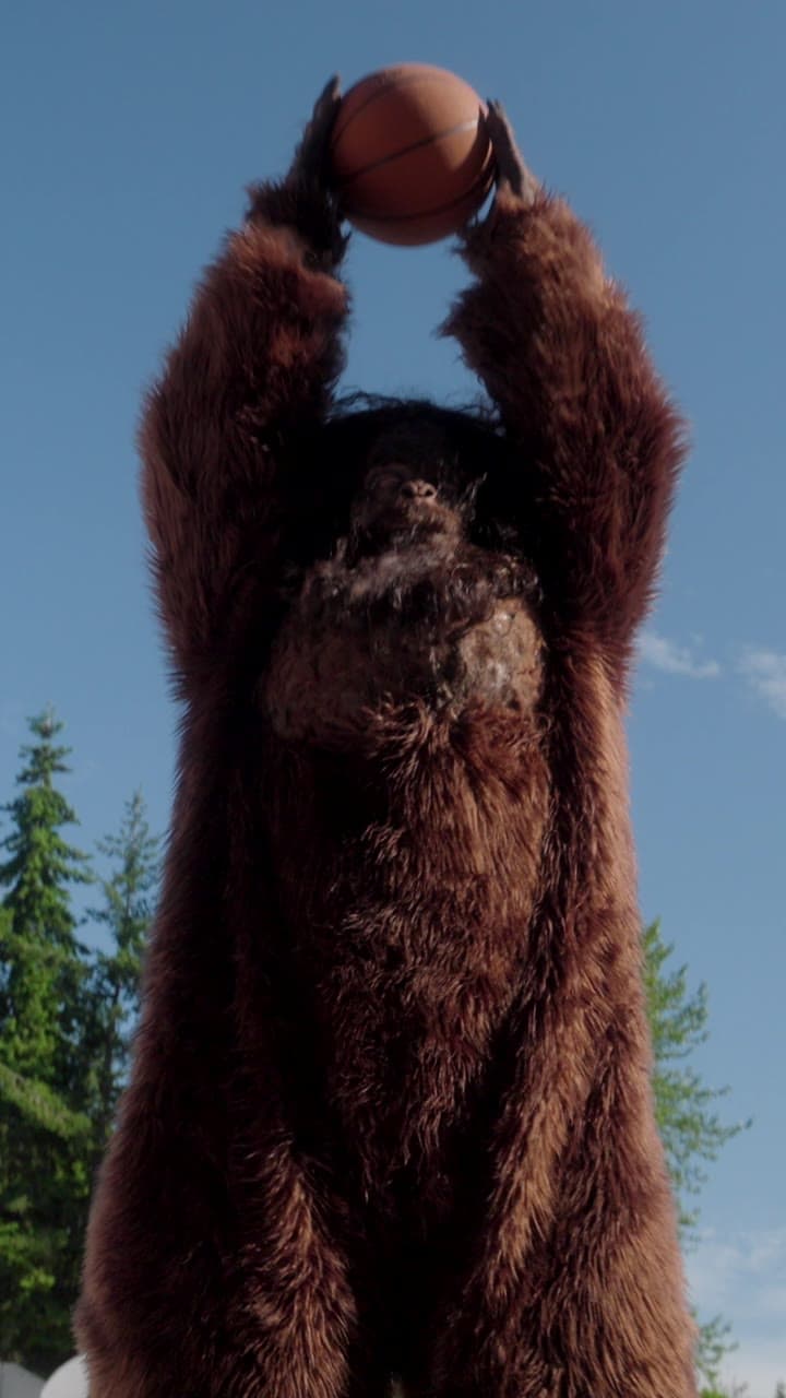 Bigfoot holding a basketball overhead against a blue sky